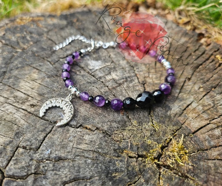 Purple beaded bracelet with silver crescent moon charm and copper wire accents on weathered tree stump