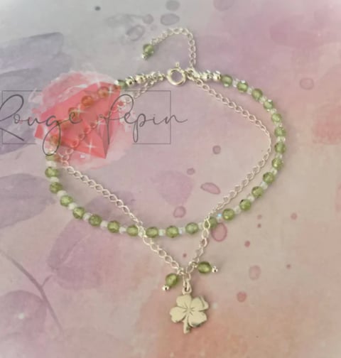 Green beaded bracelet with four-leaf clover charm and silver chain on pink watercolor background